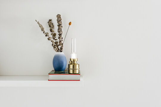Decorative objects and a quinque on a book that in turn is on a white wall shelf
