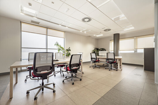 Professional office with large windows, technical ceilings, wooden meeting tables and identical swivel chairs