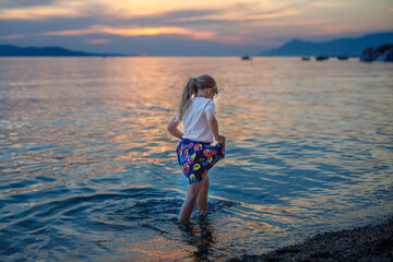 Fototapeta na wymiar Little girl walking on beautiful ocean beach. Happy preschool child play by sunset on sea beach. Family vacations with children in summer.