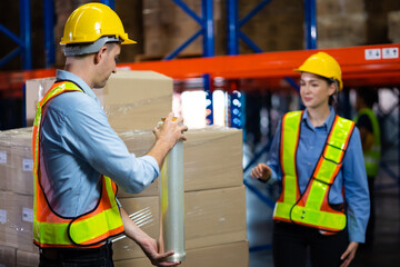 Caucasian team man and woman worker working at warehouse factory. Warehouse staff worker are helping to wrap the shock absorber on the container box