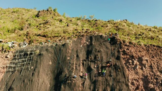 Protection of road from mountain slough, rockfall with metal accumulative restraining net fences. Workers constructing anti-landslide concrete wall prevent protect against rock slides. Rockfall