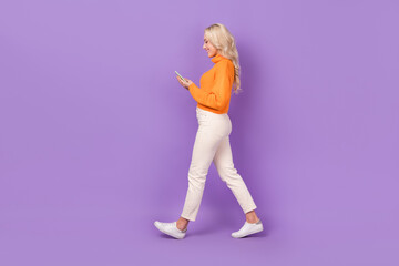 Fototapeta na wymiar Full size profile photo of cheerful pretty girl hold use smart phone walking isolated on violet color background