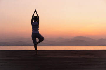 Fototapeta na wymiar Full length rear view of woman standing on one leg while doing yoga at sunrise.