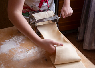 Cooking fresh homemade pasta: top view of a woman's hand pulling out the rolled dough from a manual...