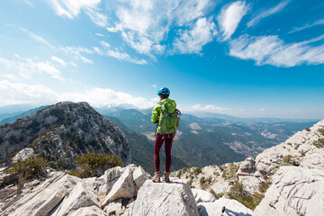 Fototapeta premium Woman climber with a backpack and a helmet in the mountains. A girl with a backpack walks along a mountain range. adventure and mountaineering concept.