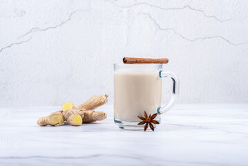 Masala tea in a glass mug, ginger root and cinnamon with star anise.