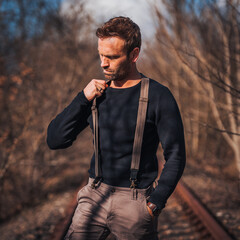 Male model is looking down while grabbing his suspenders