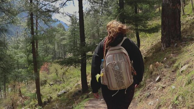 woman walking in a forest trail with a backpack  - Parvati Valley - Himachal Pradesh - Himalayas, India