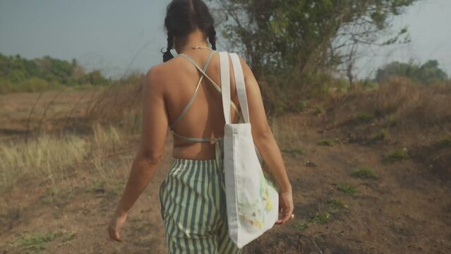 Young Indian women wearing a backless top walking on a pathway holding shoulder bag