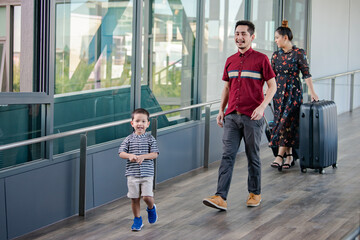 Little boys looking camera, having fun  and going on vacations trip with Joyful asian middle parents walking with suitcases while going to flight departure gate.