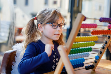 Little preschool girl playing with educational wooden rainbow toy counter abacus. Healthy happy...