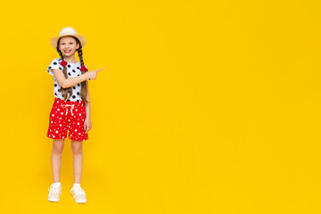A beautiful girl dressed in summer clothes points to an empty copy space highlighted on a yellow background.