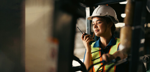 Indian woman worker driving a forklift and using a walkie-talkie at warehouse factory container. communication radio. Inventory and wholesale concept © NVB Stocker