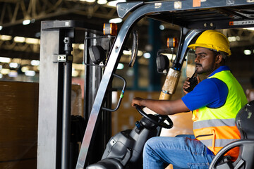 Talking on radio walkie talkie. Indian man worker driving a forklift at warehouse factory....