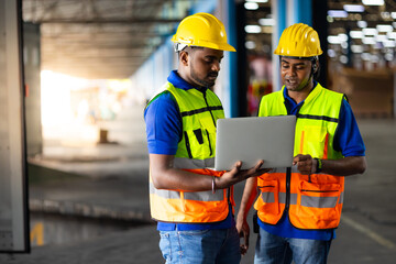 Two men warehouse indian worker wearing safety hardhats helmet working on laptop computer in warehouse of Wholesale Merchandise. shelves, pallets and boxes. Container and warehouse factory