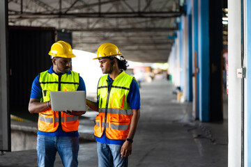 Two men warehouse indian worker wearing safety hardhats helmet working on laptop computer in warehouse of Wholesale Merchandise. shelves, pallets and boxes. Container and warehouse factory