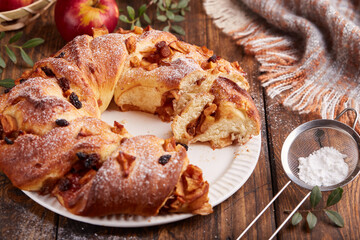 Yeast dough wreath pie with apples, cinnamon and raisins covered with sugar powder. Braided ring shaped cake.