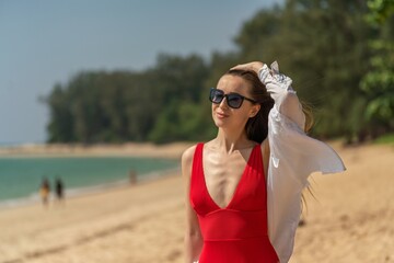 Beautiful caucasian female sexy woman lady in red swimsuit bikini on the beach with black sunglasses enjoying the sun tan and sea breeze happily. Happy holiday!