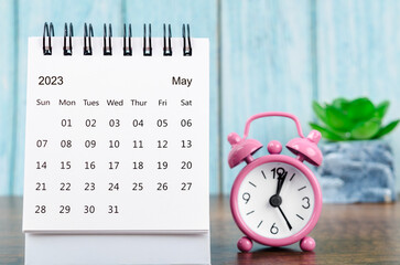 The May 2023 Monthly desk calendar for the organizer to plan 2023 year with pink alarm clock on wooden table.