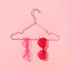Valentines day creative layout with heart shaped sunglasses on clothes hanger on pastel pink...
