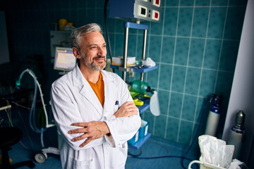 A male doctor standing in the examination room and looking through the hospital window.