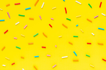 flat lay of colorful sprinkles over yellow background, festive decoration for banner, poster, flyer, card, postcard, cover, brochure, designers