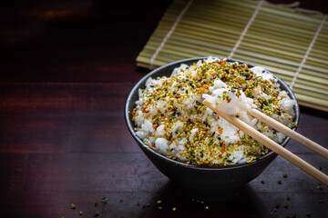 close up rice with Japanese spices in black bowl and chopsticks on wooden background, copy space, traditional Asian food