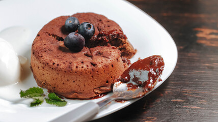 petit gâteau, chocolate fondant, dessert composed of a small chocolate cake with crunchy rind and mellow filling that is served hot with vanilla ice cream on a plate.