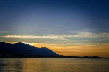 Fototapeta premium sunset on the sea bright sky with clouds on the left you can see the mountains no longer lit by the sun and the orientation is landscape there is a place for text