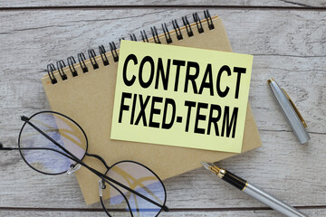 Fixed-Term Contract symbol. text on a yellow sticky note on the desk next to the glasses.