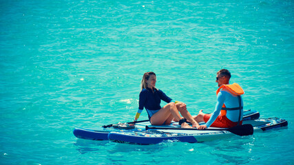 Man and woman sitting on a stand up paddle boards. Couple taking time together relaxing on sup boards