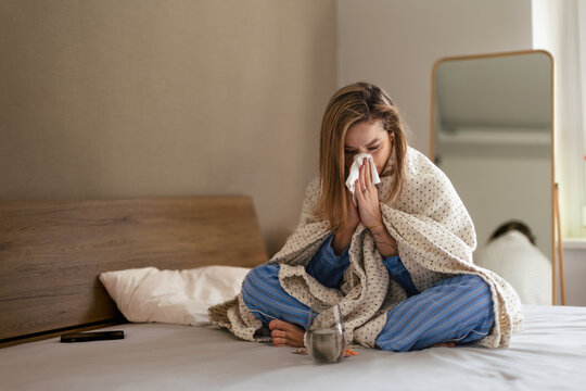 Sick woman sitting on a bed with blanket.