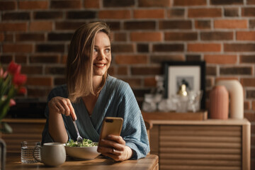 Young woman eating salad and scrolling her phone.