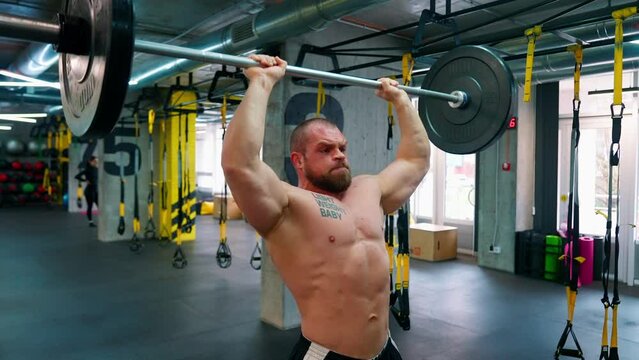 Bald bodybuilder exercising in the gym. Raises the barbell, dumbbells, jumping rope, trx workout. Pumped up big muscles. Work with large, heavy weights in the gym. Nice curvy body.