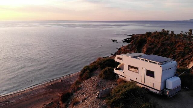 Aerial view. Camper rv with solar photovoltaic panels on roof camping on cliff sea shore at sunrise. Mediterranean region of Villaricos, Almeria, eastern Andalusia, Spain.