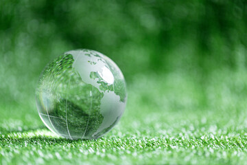 Close up of crystal globe resting on green grass with blur nature background, earth day or world environment day concept. Green world and sustainable conservation of forest resources.