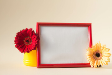 Empty photo frame with red and yellow gerbera daisy flowers on pastel beige background.  Picture frame mockup with flowers, Copy space.