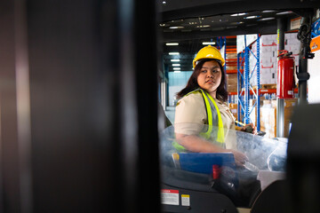 Fototapeta premium Asian fat female warehouse worker drive forklift in warehouse. Warehouse staff worker by goods shelf working in large warehouse factory