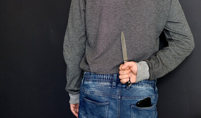 Man wearing grey long-sleeved shirt hides a knife behind his back. Domestic violence concept. 