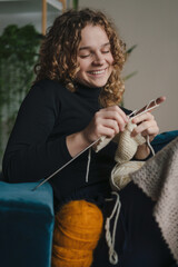 Happy young woman sitting on sofa at home enjoying leisure activity, knitting. People inner lifestyle hobby. Domestic lifestyle. Happy lifestyle.