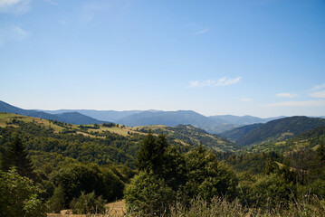 Fototapeta premium Natural landscape in the mountains in summer. Sunny rural scenery with bright blue sky. Nature protection concept. Green tourism in ukrainian village. Breathtaking mountain view.
