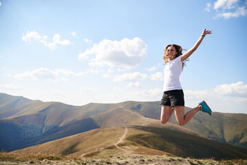 Young woman jumping on top of the mountain. Feeling happy and free. Natural landscape in summer. Sunny rural scenery. Nature protection concept. Breathtaking mountain view.. On top of the world