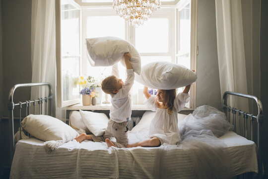 Cute boy and girl fighting with pillows in cozy room.