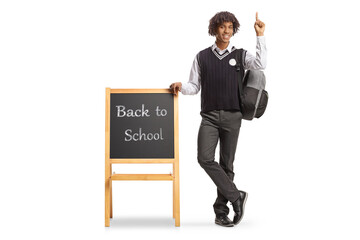African american student in a uniform leaning on blackboard with text back to school and pointing up