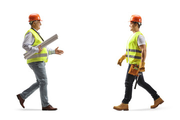 Full length profile shot of an engineer carrying blueprints and greeting a construction worker