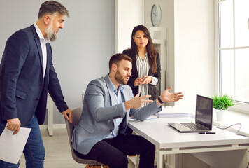 Business team having a work meeting in the office. Young man talking to his colleagues, explaining something, and showing some graphs and charts on a laptop computer