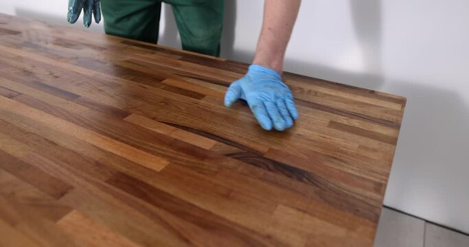Closeup of carpenter hands covering wooden surface with protective varnish. Carpentry varnishing of a piece of furniture
