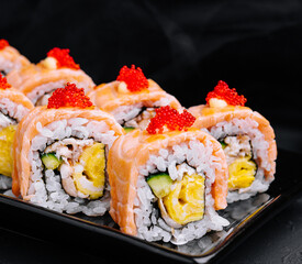 Sushi roll with fried salmon on black plate