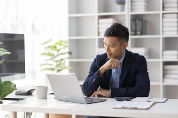 Fototapeta na wymiar Focused young adult businessman, asian man sitting at his desk making sure his company is earning enough money financial planning concept