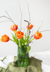 A very beautiful spring bouquet in a green vase stands on a table on a linen tablecloth, orange peony tulips. Mother's Day, March 8, Valentine's Day.